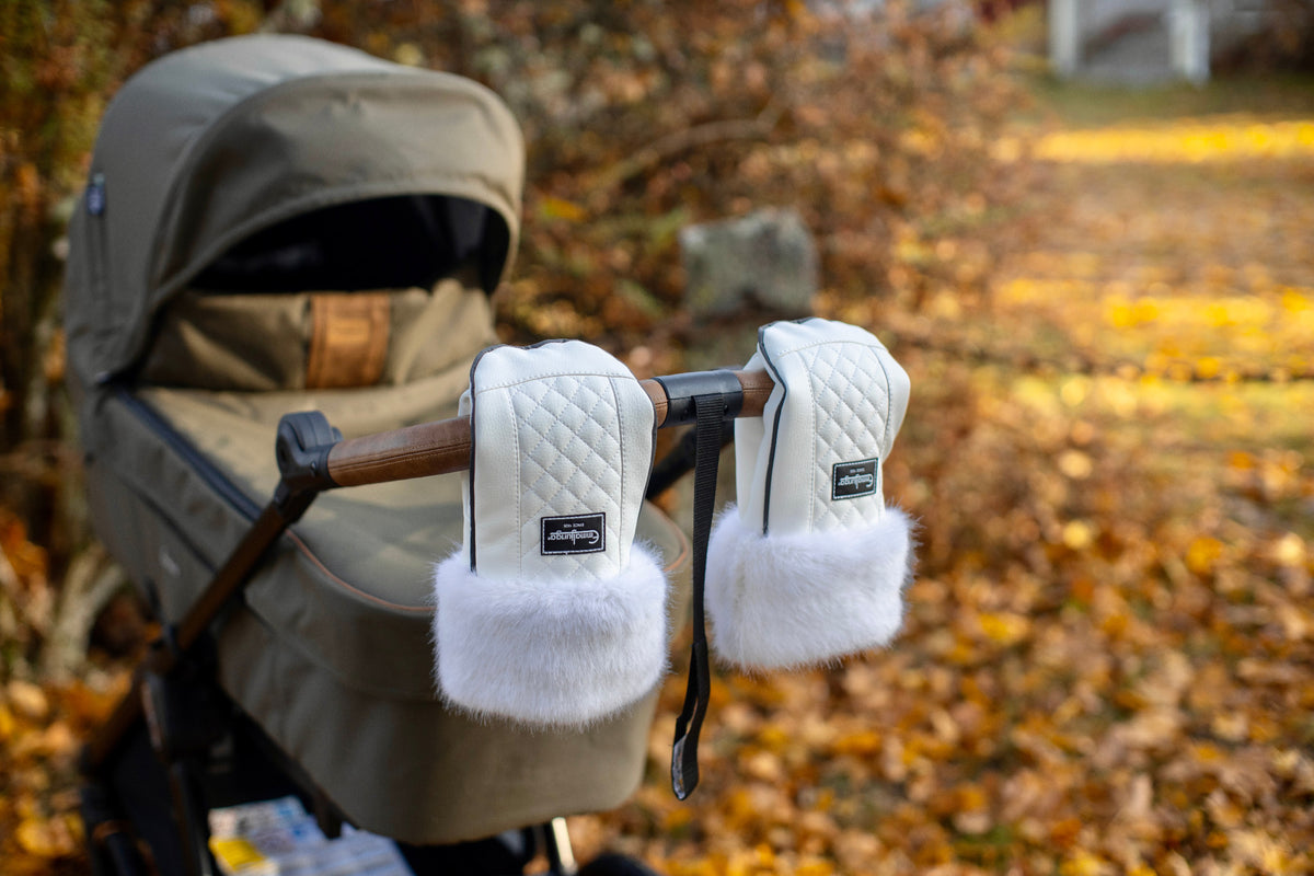 White Emmaljunga winter gloves attached around a stroller handle