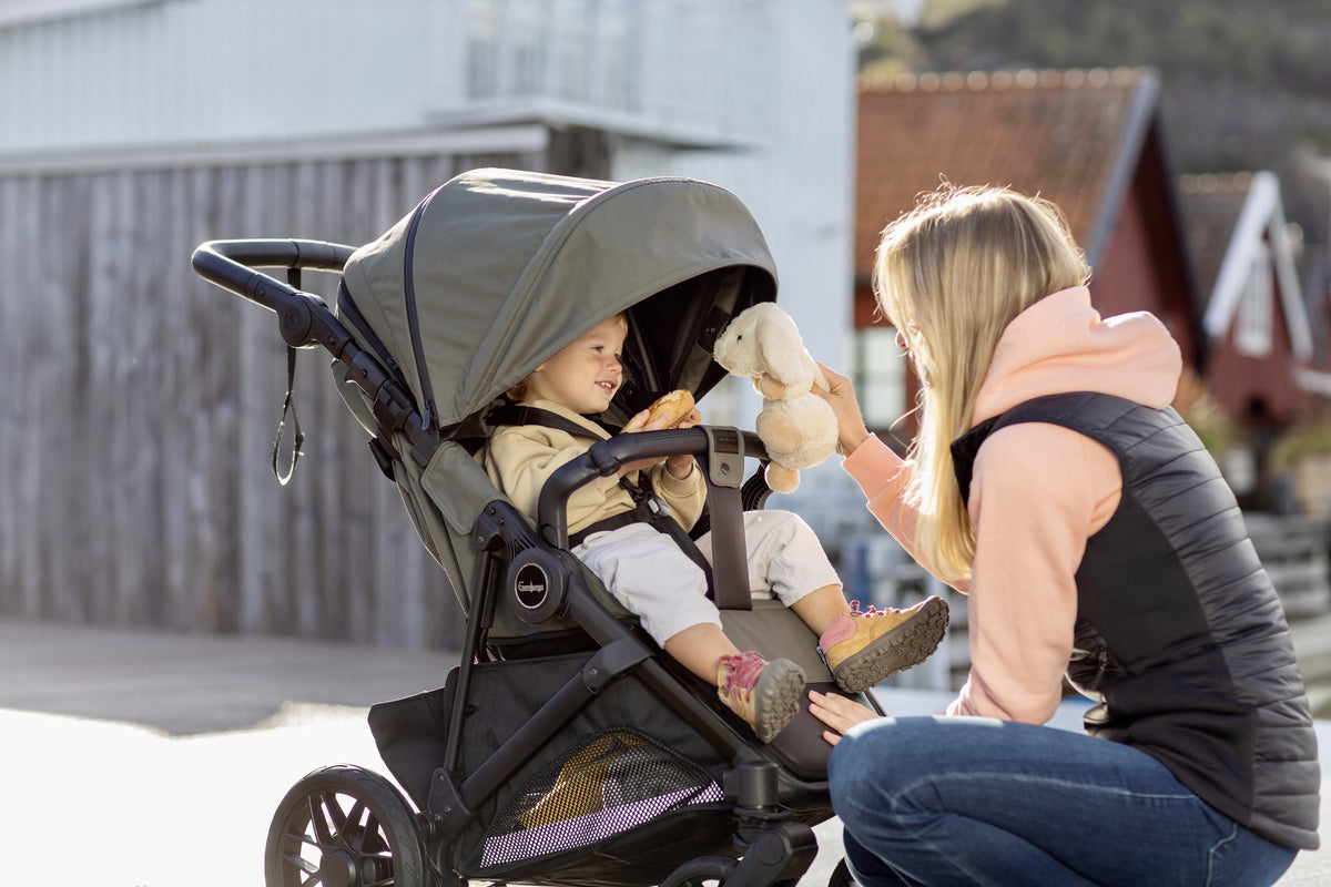 Child seated in a green stroller beside an adult at the harbour
